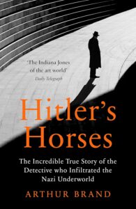 A silhouetted man in a trench coat and hat stands on steps near a curved wall. Arthur Brand’s name and the title Hitlers Horses appear in bold orange text, with a subtitle highlighting the art detective’s investigative work.